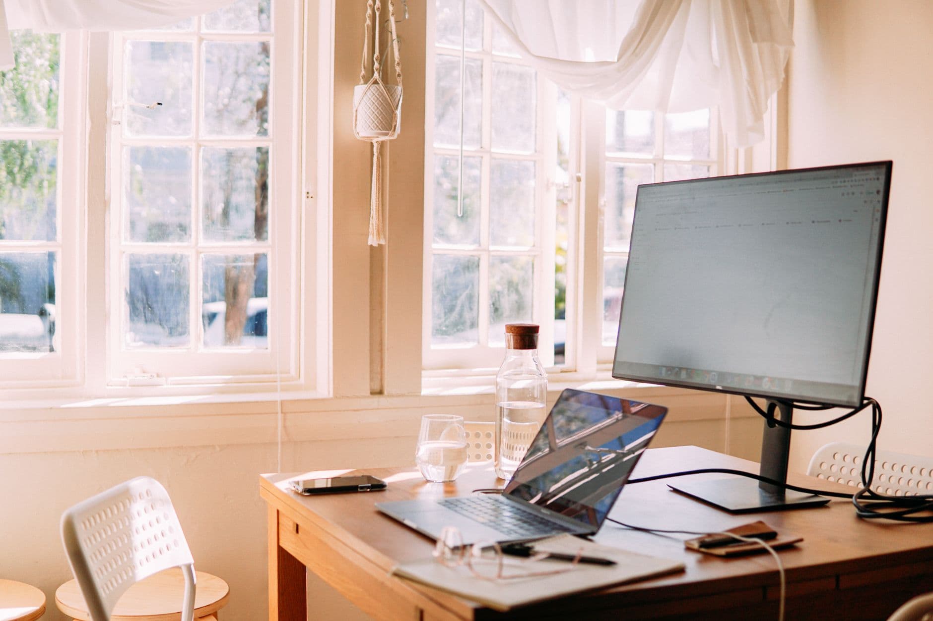 Arbeitsplatz mit Laptop an einem Holztisch, Tageslicht durch ein großes Fenster.